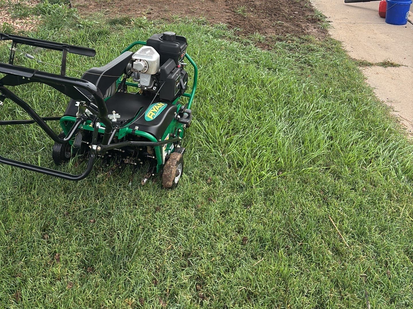 A core aerator on a Pueblo front lawn, with plug rows behind it on a foggy fall morning