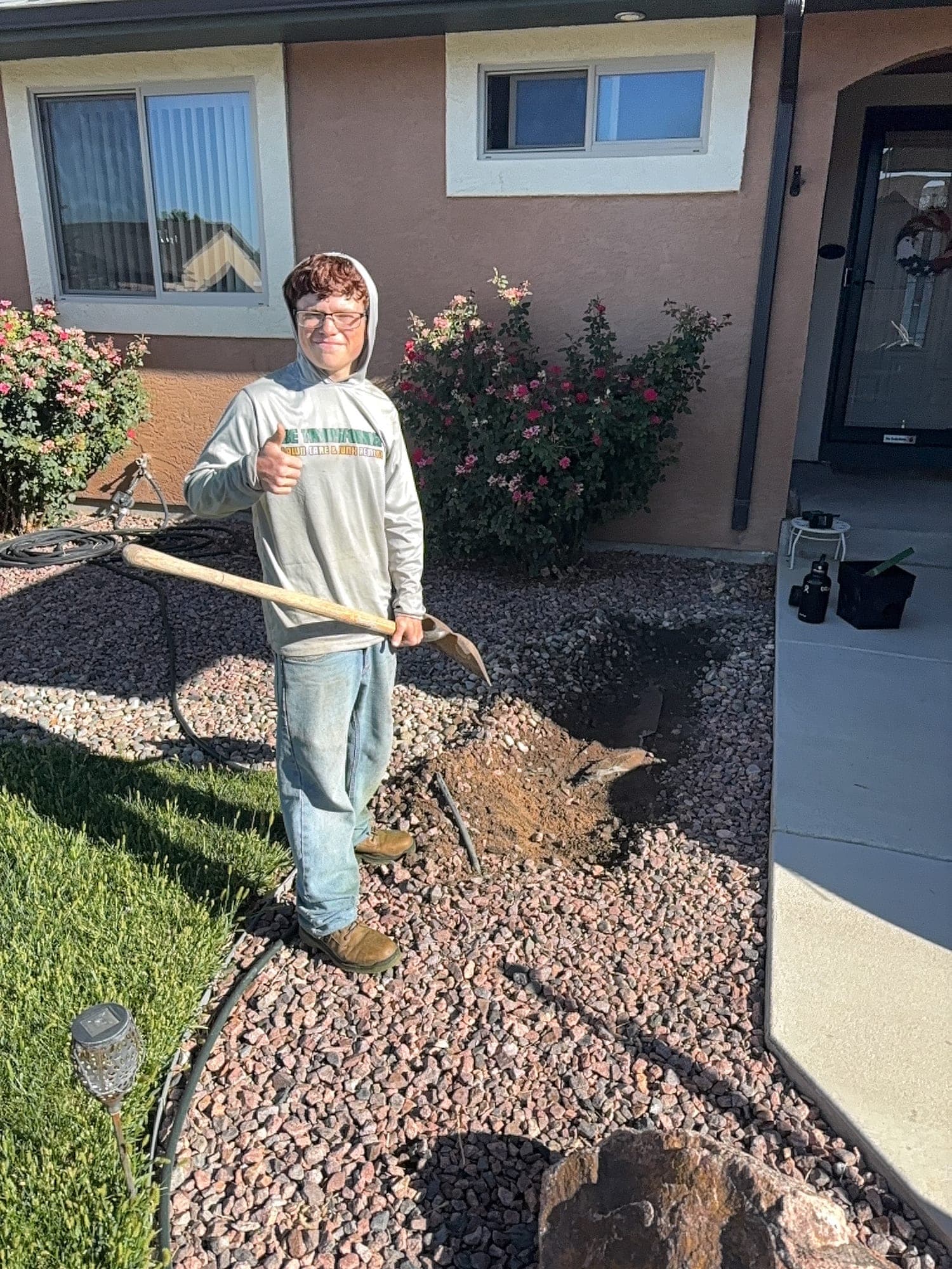 Crew member in a Be Transformed hoodie giving a thumbs up while installing drip line in a red rock bed