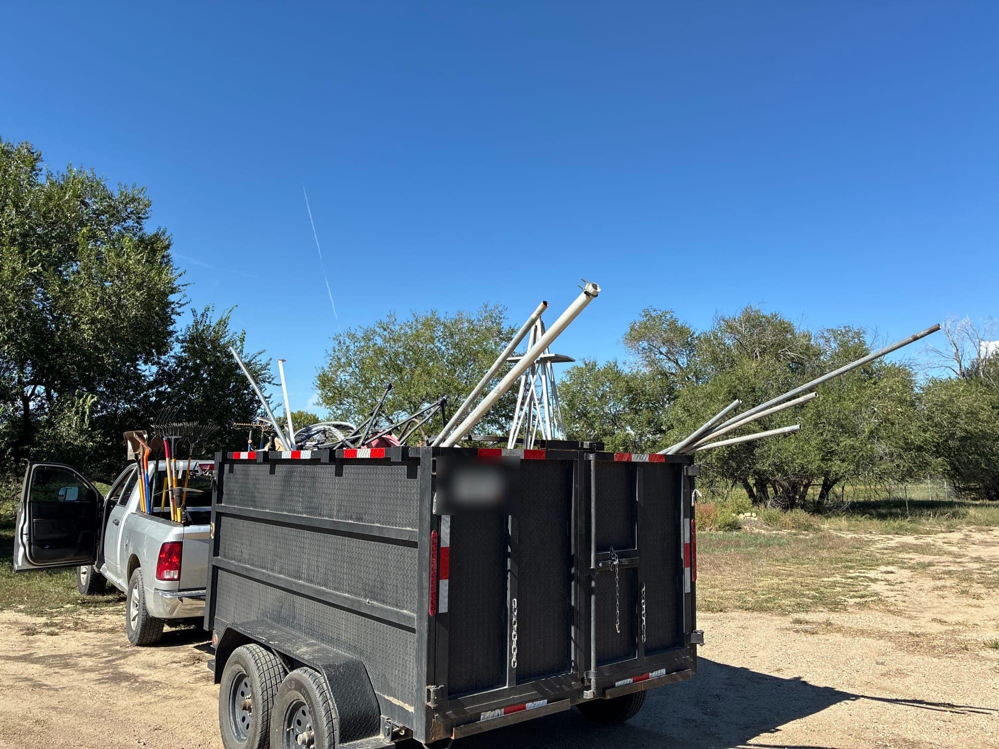 A loaded dump trailer hitched to a pickup, long poles sticking out the top, ready to haul junk from a Pueblo property