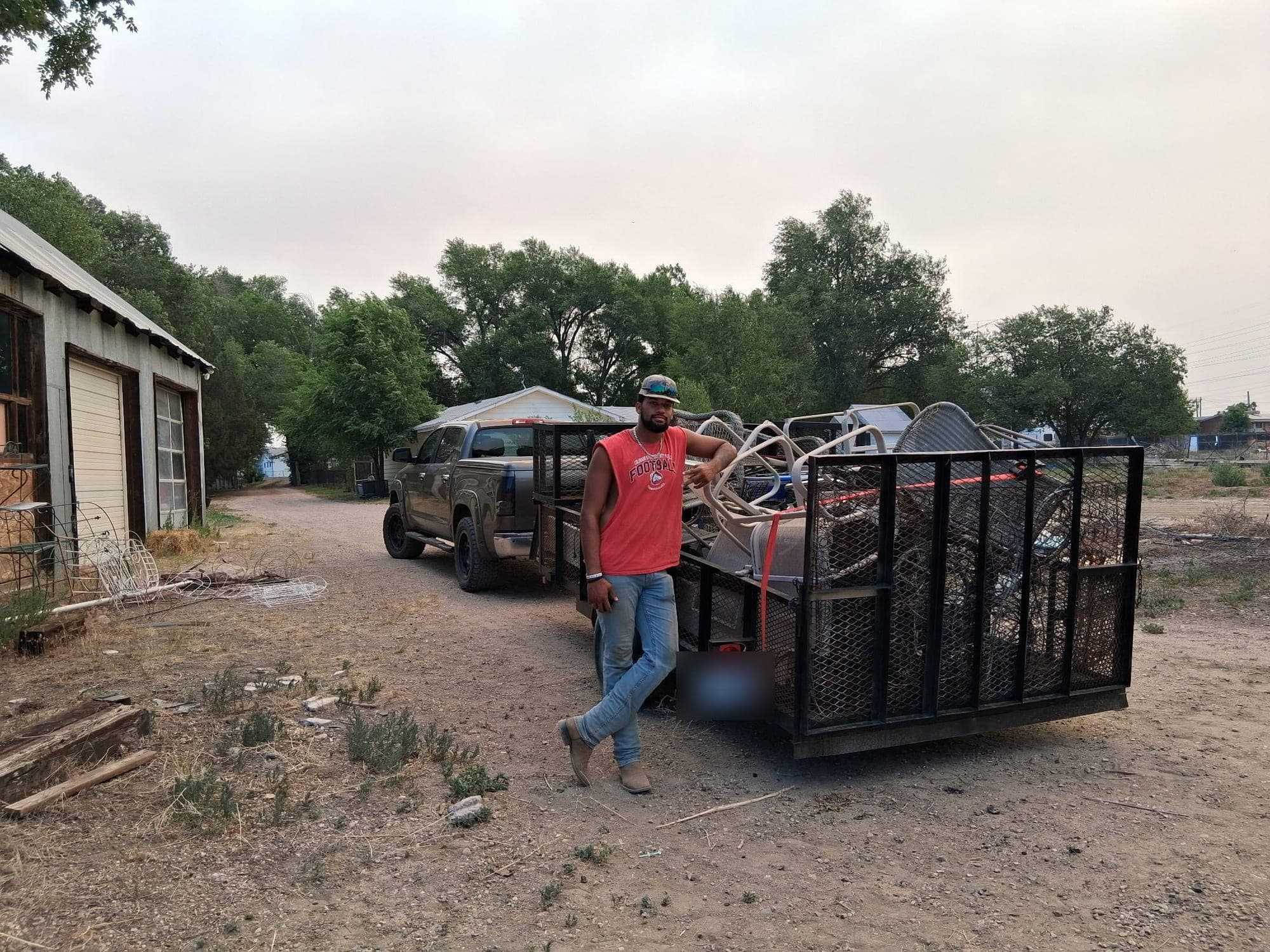 Crew member beside a utility trailer loaded high with scrap metal and old furniture from a Pueblo property