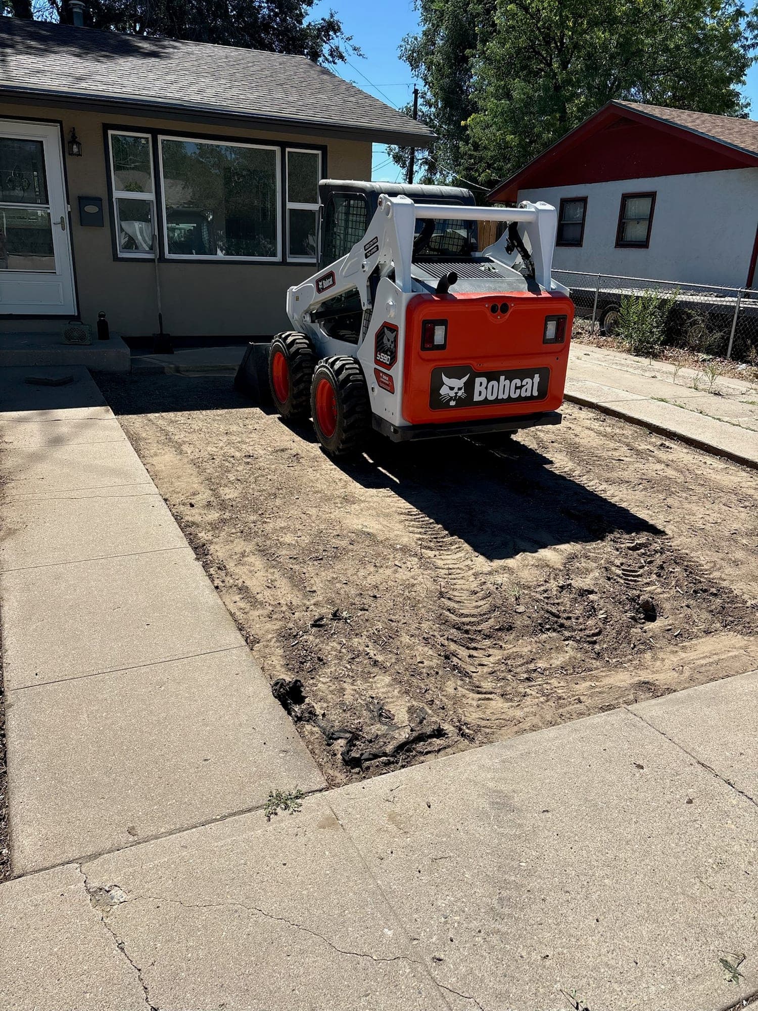 Before: a Pueblo front yard stripped to bare dirt with the skid steer parked by the walkway