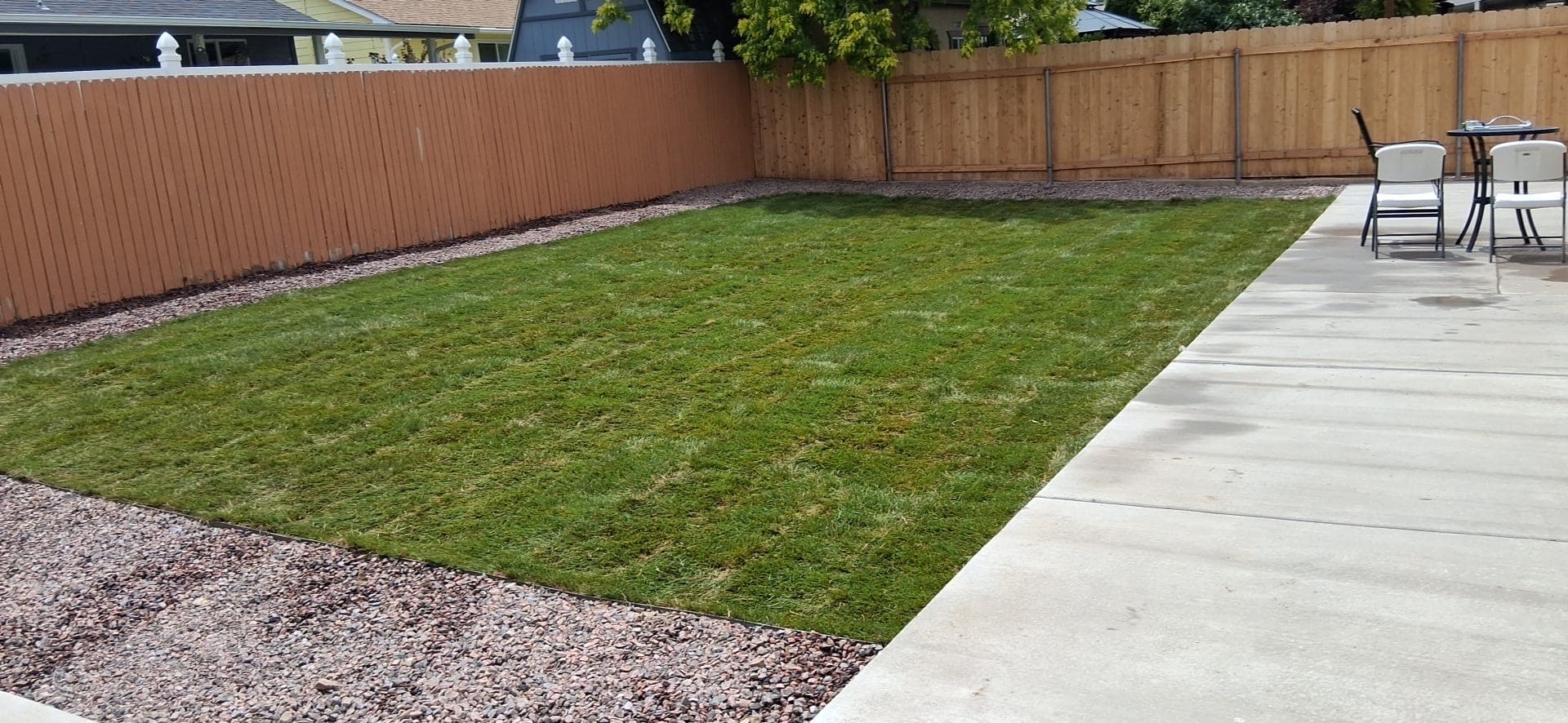 After: the same Pueblo backyard with fresh green sod, a pink rock border and the patio set back in place
