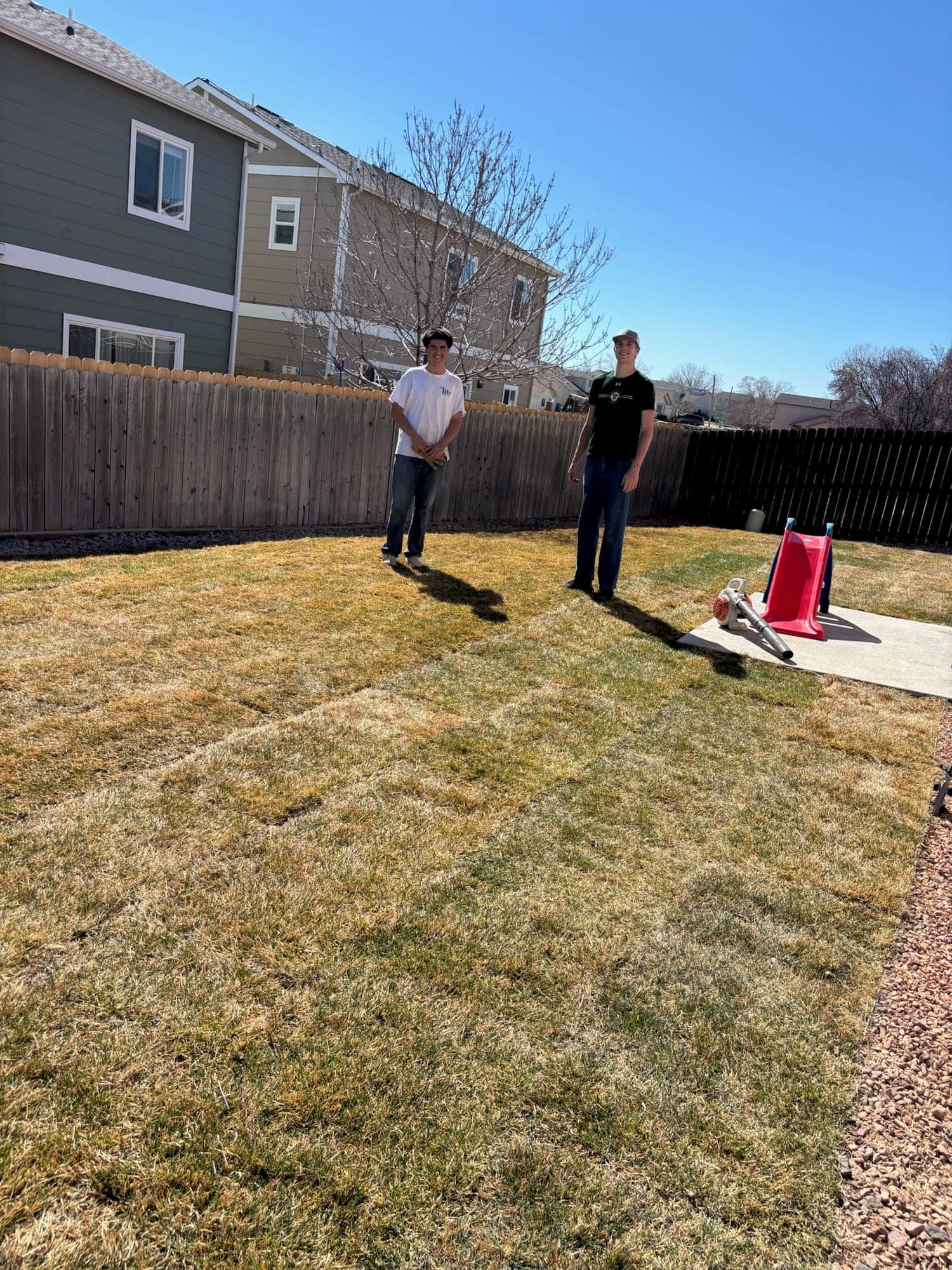Two crew members with a leaf blower on a freshly striped spring lawn in Pueblo