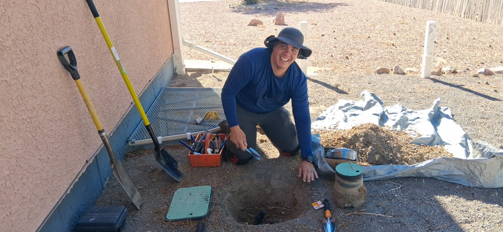Smiling crew member kneeling at an open sprinkler valve box with tools laid out on the lawn